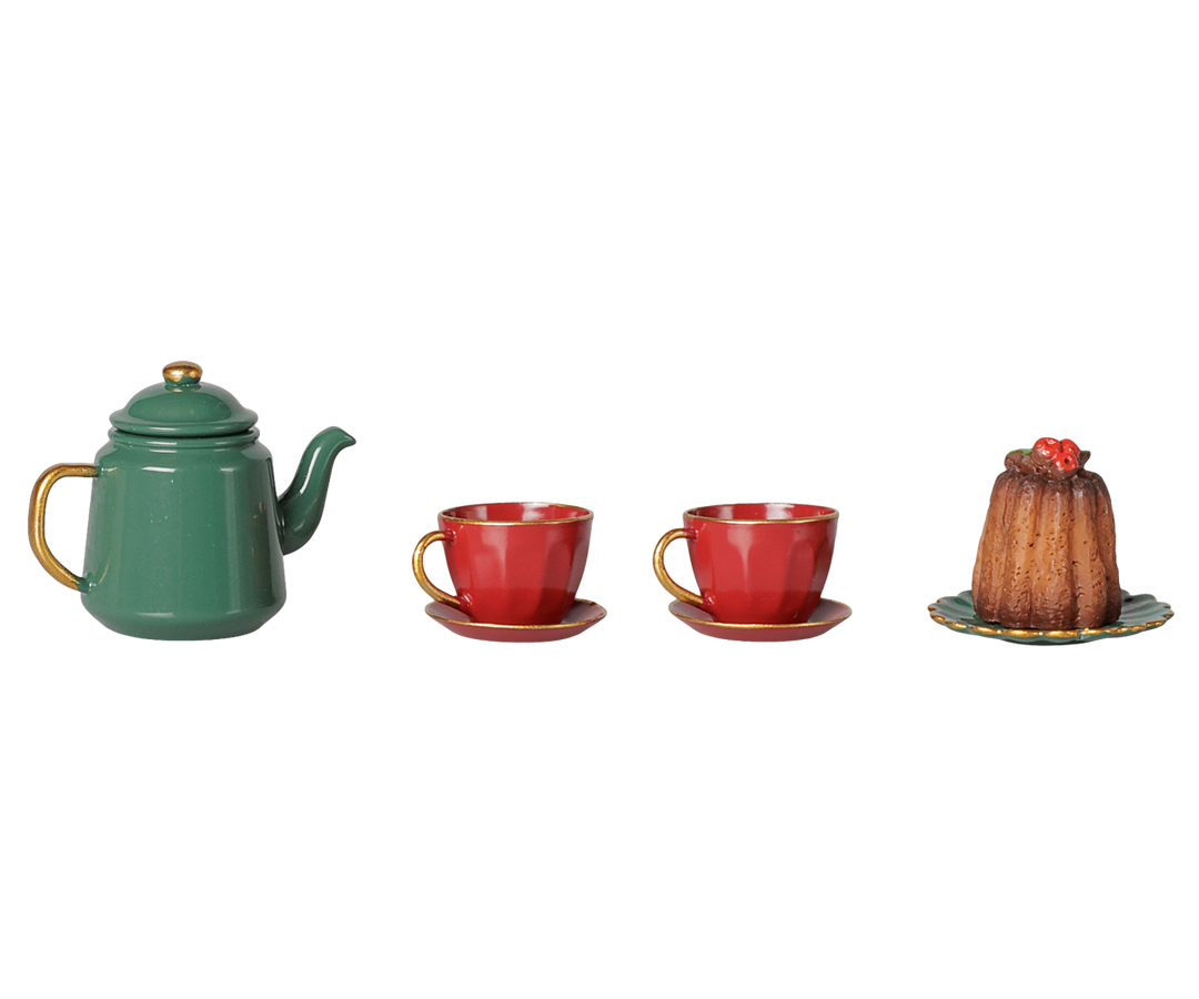 A miniature tea set and dessert display featuring a green teapot with gold accents, two red teacups with saucers, and a small brown pudding on a plate, arranged on a plain white background.